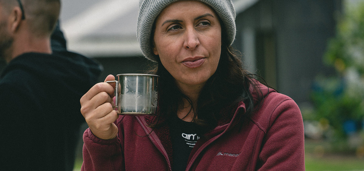 Woman wearing a grey beanie and maroon sweater holding a meta camping mug