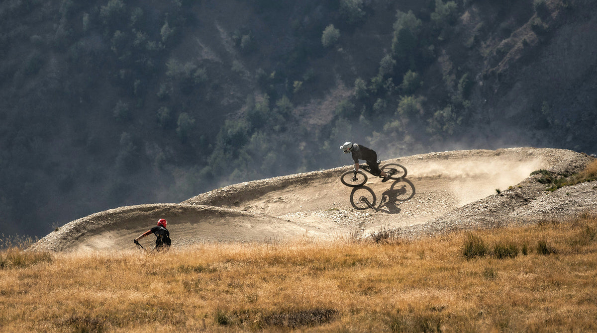 Two mountain bikers on a dirt track with a mountainous background